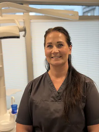 Kvinne med langt hår smiler i et profesjonelt rom, sannsynligvis en klinikk.